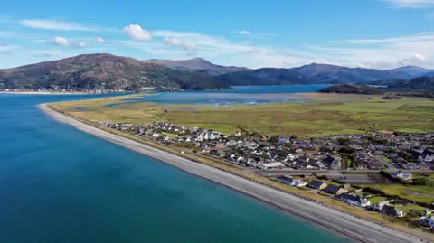 Getty Images An ariel shot of Fairbourne. The village is on the coast, which curves around, and houses and roads can be seen with a stretch of grass behind it. A mountain range can be seen in the horizon. 