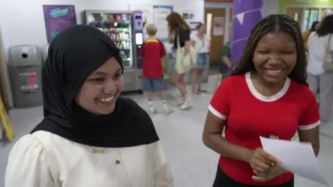Two women smile widely at someone off camera