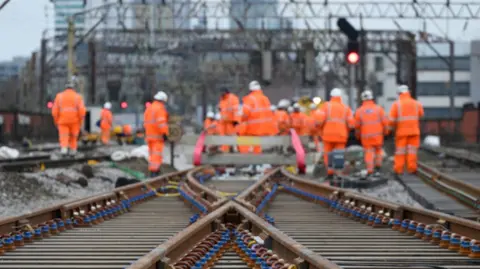 Network Rail Photograph of workers on the railway tracks close to Manchester Piccadilly Station. The image shows people in orange suits and white hats.