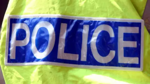 Barnaby Perkins/BBC The back of a high-visibility jacket displaying the word "Police". 