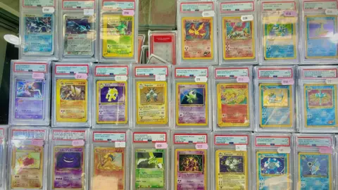 Danny Fullbrook/BBC Tiga baris kartu Pokemon. Baris atas memiliki 7 kartu, dua lainnya memiliki delapan. Ini adalah campuran warna yang berbeda. Semua disegel dalam plastik yang dinilai. Mereka memiliki nilai yang macet pada mereka, masing -masing bernilai ratusan pound.