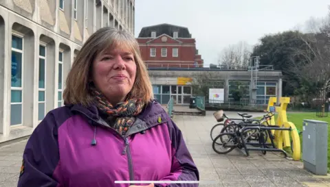 Diana Moore is wearing a thick knitted scarf and a purple and pink waterproof jacket.