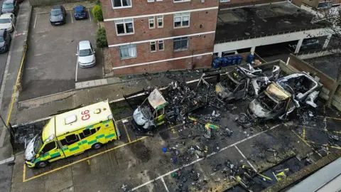AFP via Getty Images An aerial image shows burnt out ambulances in a parking area. Three vehicles at to the right are almost completely destroyed. There are cars and the lower levels of a block of flats visible at the rear of the frame.