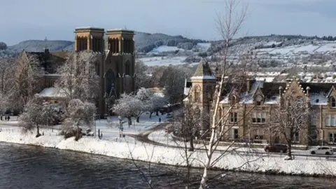 A view across the river ness on a winter's day. We can see the river in the foreground with Inverness Cathedral in the background surrounded by snow covered streets. 
