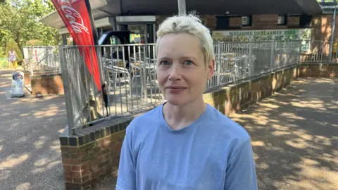 Paula Shapland in a blue t-shirt stood at the front of her cafe looking at the camera.