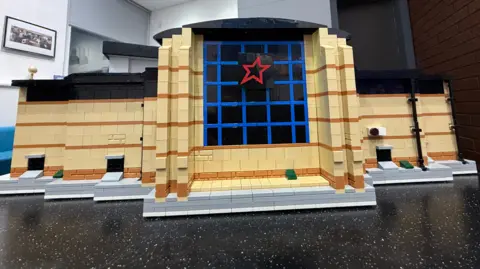 A Lego model of a Cineworld building complete with the red star logo on the front. 