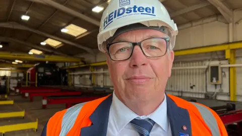 Simon in his factory with a hard hat and hi-vis vest.