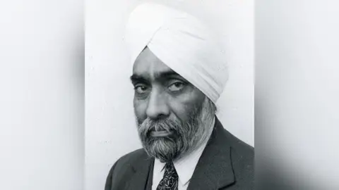 Black-and-white undated portrait image of Gyani Sundar Singh Sagar, also known as Gyani Ji. He has a beard and is wearing a turban as well as a dark suit and tie and white shirt.