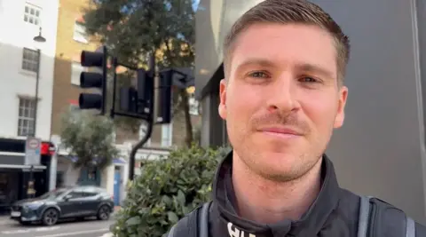 Luxmy Gopal/BBC Lochlan Dinhim in a black coat and wearing a rucksack. 