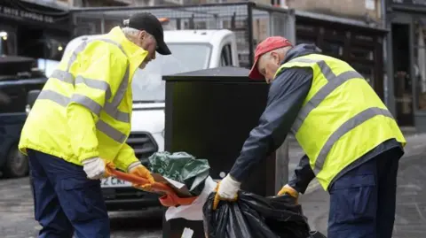Two refuse collectors shovel rubbish into bin bags in Edinburgh