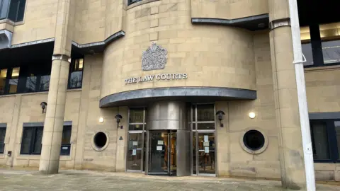 The main entrance to a modern-looking building made of stone. Above a steel revolving door is a sign and coat of arms which states THE LAW COURTS. There are stone columns on either side of the doors.