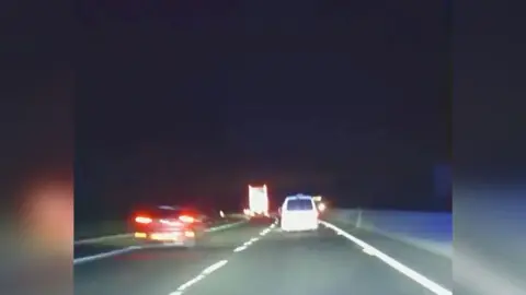 White van drives down A421 at night at speed overtaking a red car and approaching a lorry