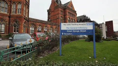 Getty Images A general view of Leeds General Infirmary hospital. Members of the public walk up the path to the main building. A blue and white NHS sign stands in the foreground.