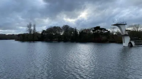 BBC Weather Watchers/SSMani A lake on a cloudy day with silhouettes of trees in the background. A tall white viewing platform looks over the lake. 