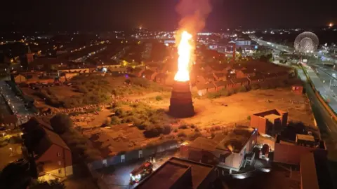 PA Media Bonfire alight at a site off the Donegall road in south Belfast. A Northern Ireland Fire and Rescue Service appliance is located beside an electricity substation.