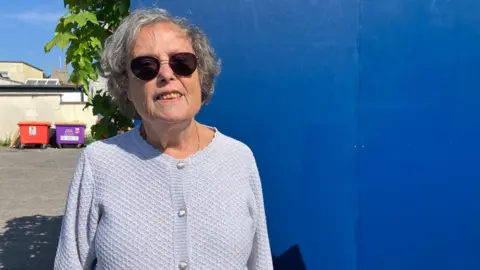 A woman wearing sunglasses stood in front of a blue wooden wall.