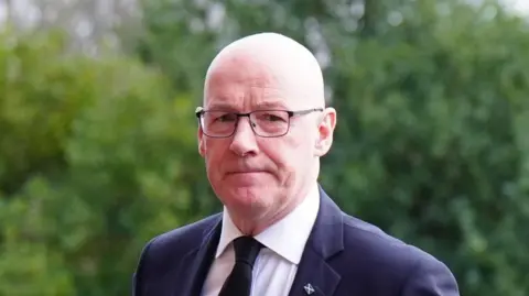 PA Media John Swinney, who has a bald head and glasses, is looking at the camera. H is wearing a dark suit with a white shirt and dark tie.