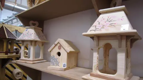 Alex Pope/BBC A number of wooden bird boxes on a shelf, in a room. They have prices on them. 