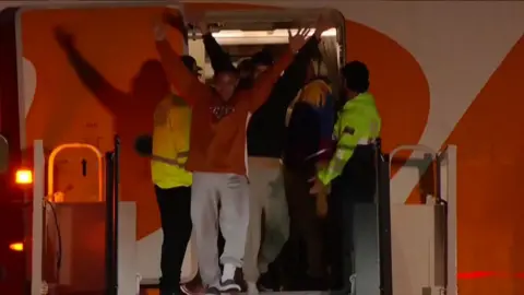 A man wearing a red sweatshirt, raises his hands in the air as he disembarks from a Conviasa plane at the airport outside Caracas.