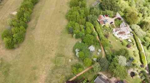 Qays Najm/BBC An aerial view of a golf course fairway, lined with trees, and a large house on the right.