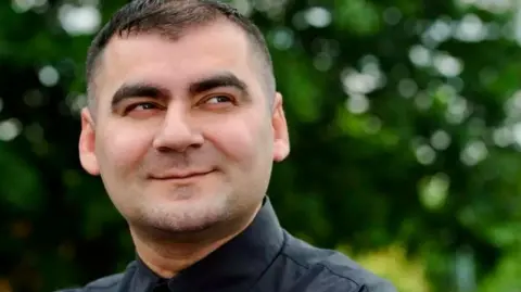 Mohammed Zafran Mr Zafran has dark hair and is wearing a dark shirt. He is smiling but looking away form the camera.