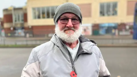 Sam Dixon-French/BBC Steve Meehan, an older man with a white beard wearing a woolly hat and grey jacket.