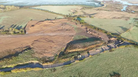 Fresh earth lies where waste was tipped six months previously and a digger prepares a trench further to the right. The Medway marshes are beyond 