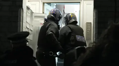 Two GMP officers batter down the door of one address during the raids. They've heavily clothed and both hold an instrument designed to open the front door.