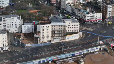 Eddie Mitchell An aerial shot showing a section of blue barriers across the road which leads to the hotel. The Royal Albion can be seen covered in scaffolding in the centre of the image. The beach is just visible in the foreground.