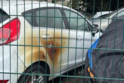 A white car, parked in a yard, with large scorch marks on the right hand passenger 