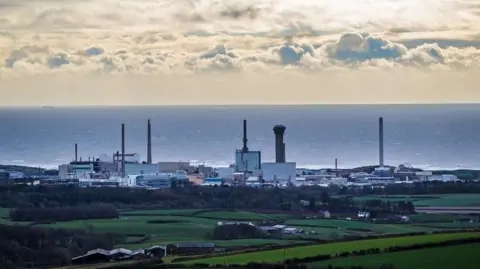 PA Media General view of Sellafield Nuclear power plant, in Cumbria. The shot is taken from a distance further away, with the sea on the horizon and a cloudy, but sunny day. The forefront is green areas of land.