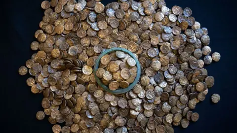 Fountain Media A pile of 933 Iron Age gold coins resting on a black background. In the middle coins are heaped around the rim of a vessel.