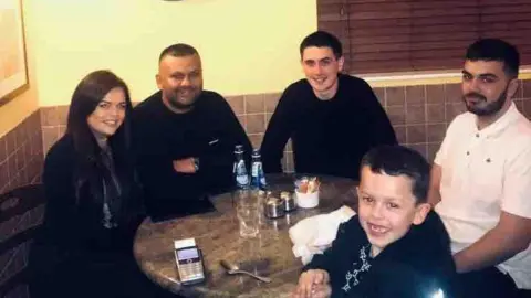 Aime A family of five sat at a dinner table in a restaurant smiling.