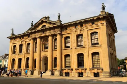 Getty Images The exterior of the large neoclassical yellow brick building. Four muses can be seen at the front of the roof.