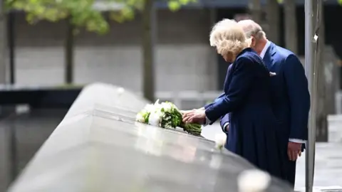PA King Charles III and Queen Camilla laying a bouquet of white flowers on the edge of one of the pools at the 9/11 Memorial