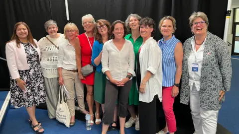 BBC 11 women standing in a row, smiling