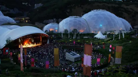 Crowds beginning to form around the stage in front of the Eden Project on a previous year, with the two, interconnected biomes in the background.