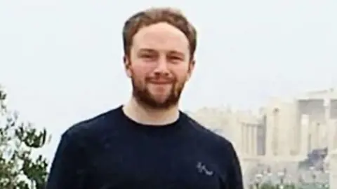 BBC Head and shoulders photo of James Denholm looking at the camera while standing outside wearing a black top