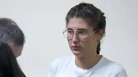 Bella Culley filmed in court. She is wearing glasses and has brown hair in a plait and is wearing a white top