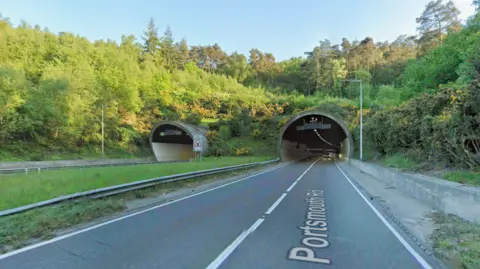 A stretch of road leading into a tunnel. It is a sunny day.
