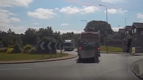 A still from a police dashcam showing a van on the wrong side of the road on a roundabout