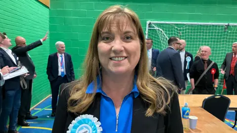 A woman wearing a Reform badge smiling.