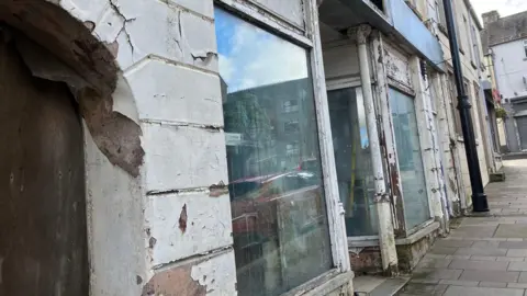 A row of derelict buildings with a butcher shop at the top of the row closed