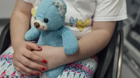 Getty Images anonymised image of child clutching a blue teddy, wearing bright red nail varnish