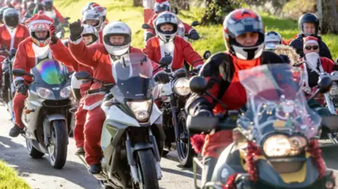 Plan.com Picture of a previous year's event with several motorcycle riders dressed as Santa driving past the camera