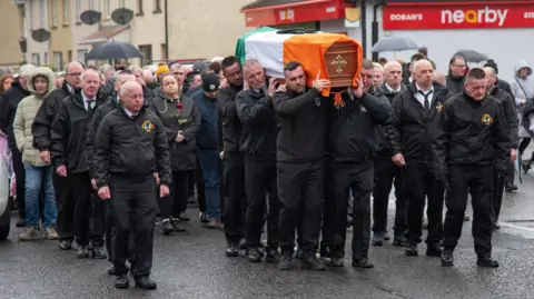 Shows men dressed in black carrying the coffin of Pearse McAuley 