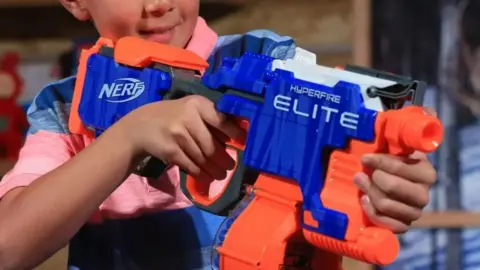 A adjacent  up   of a bluish  and orangish  Nerf weapon  being held by an unidentified child