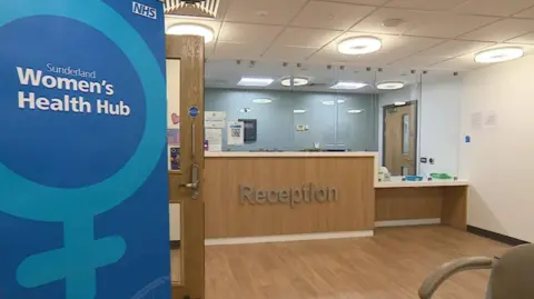 The reception area of the women's health hub. There is a blue banner on the left reading Women's Health Hub, Sunderland.