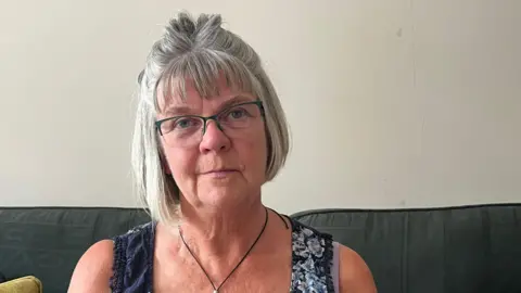 Julia Gregory / BBC A woman with grey hair sat on a sofa.