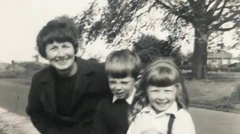 Fiona Dryden  A black and white image of a smiling woman with two young children 